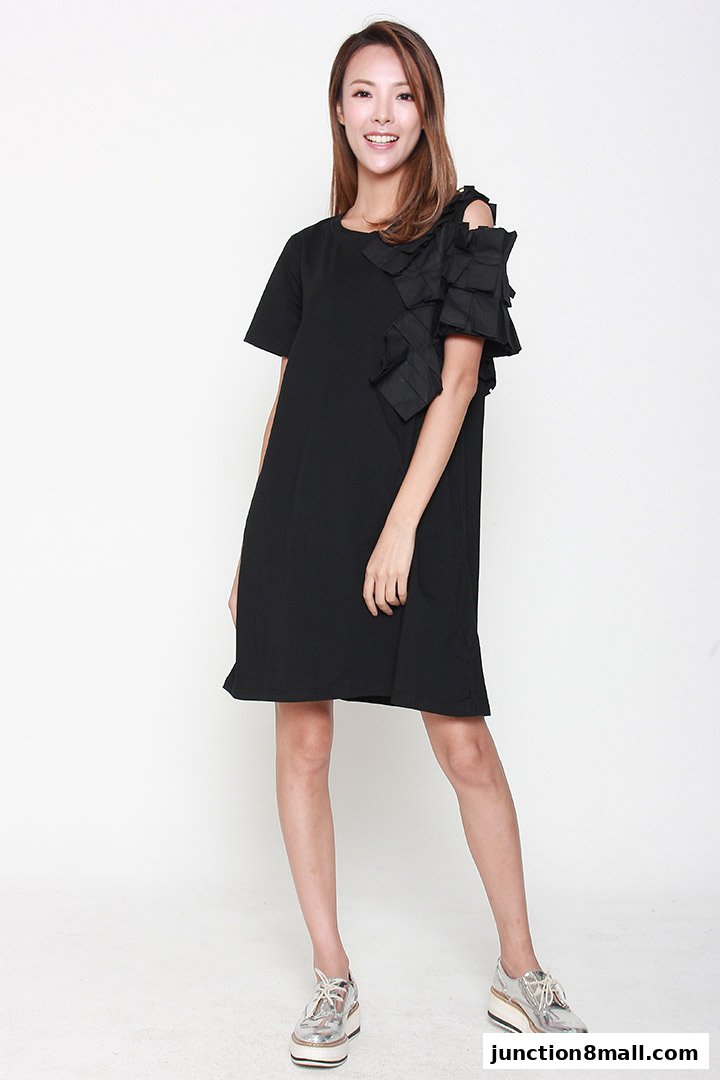 A smiling woman models a black dress with ruffled shoulder detail and silver platform shoes.