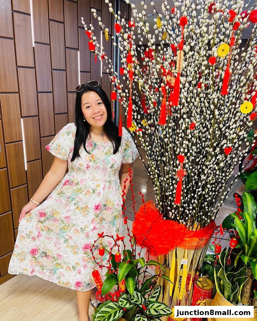 A woman in a floral dress poses next to a large decorative floral arrangement with red and gold accents.