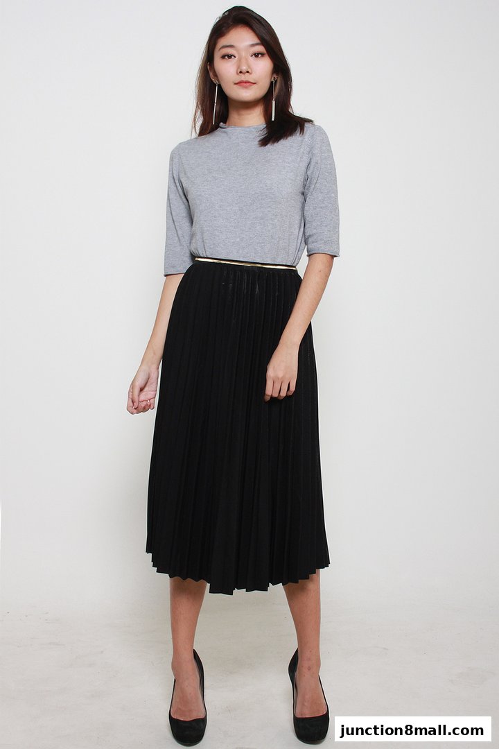 A woman models a grey top and a black pleated midi skirt with heels.