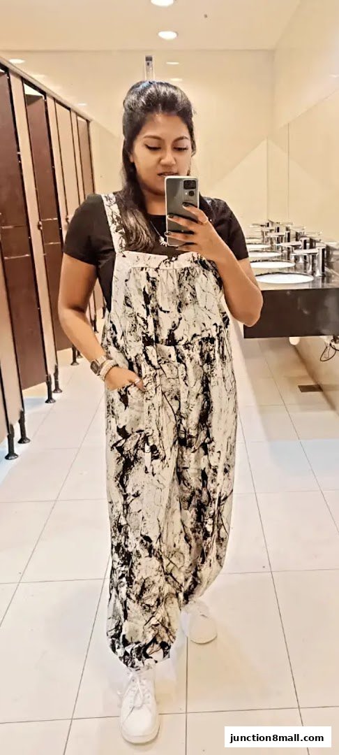 A woman in a black t-shirt and a black and white patterned jumpsuit takes a selfie.