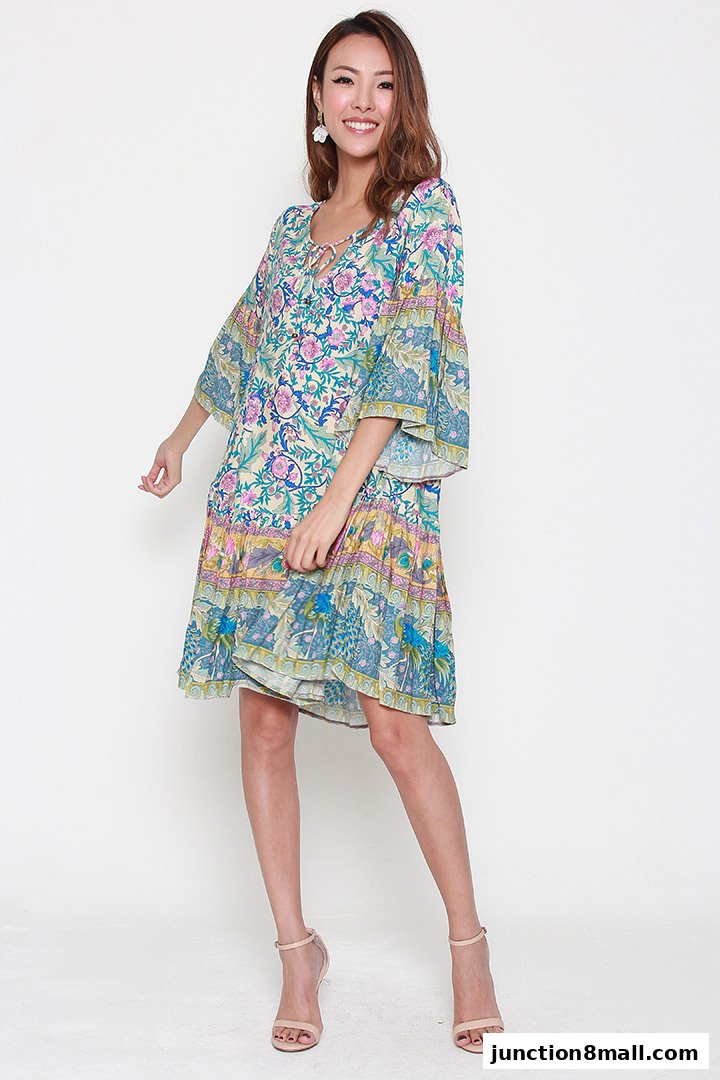 A smiling woman models a colorful, floral print, bohemian-style dress with bell sleeves.