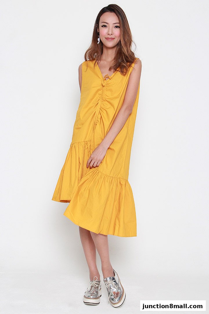 A woman models a yellow sleeveless dress with a ruffled hem and tie-front detail.