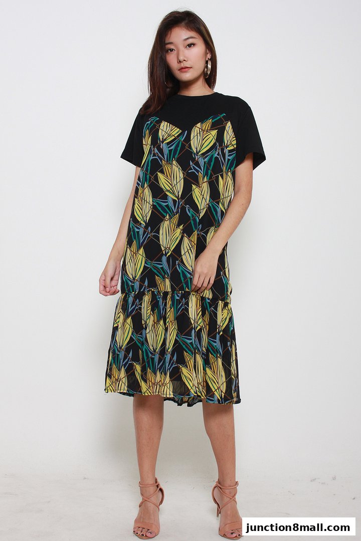 A woman models a black dress with a tropical leaf print and tiered skirt.
