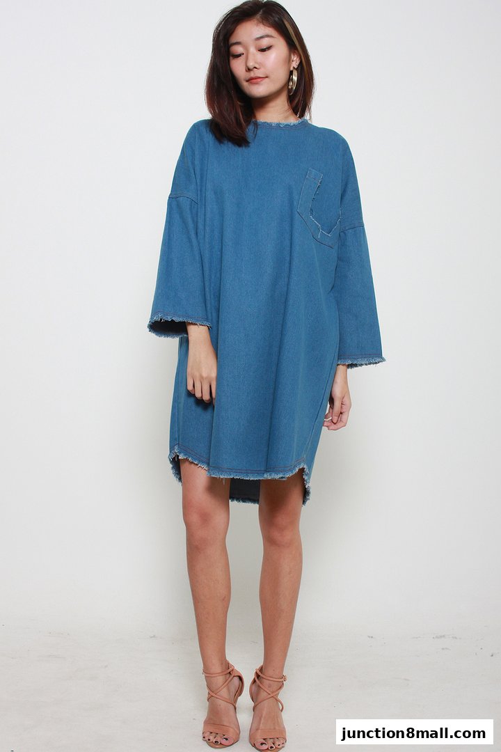A woman models a loose-fitting denim dress with frayed edges and a chest pocket.