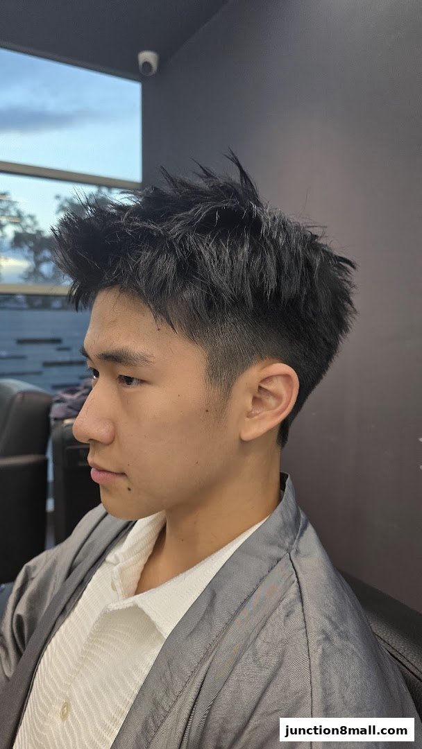 A young man with a stylish haircut sits in a salon, looking to the side.