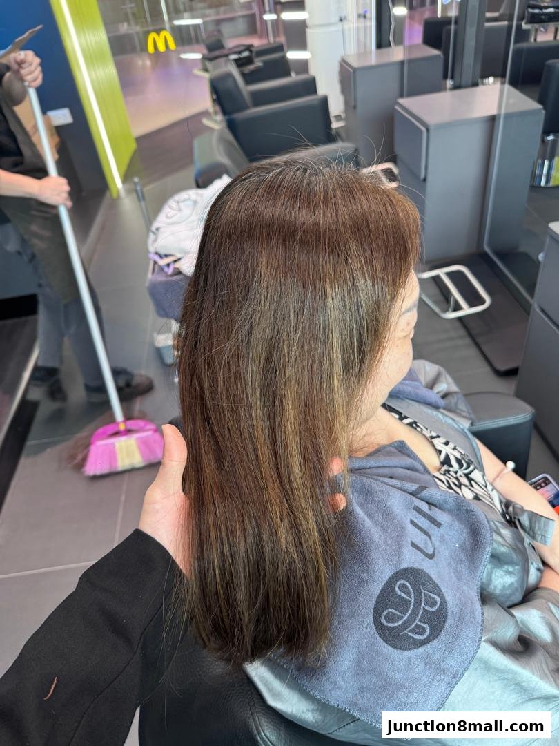 A person's hair is being styled in a modern salon with chairs and mirrors visible.