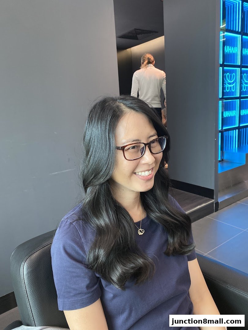 A smiling woman with styled hair sits in a salon chair, with neon signs in the background.