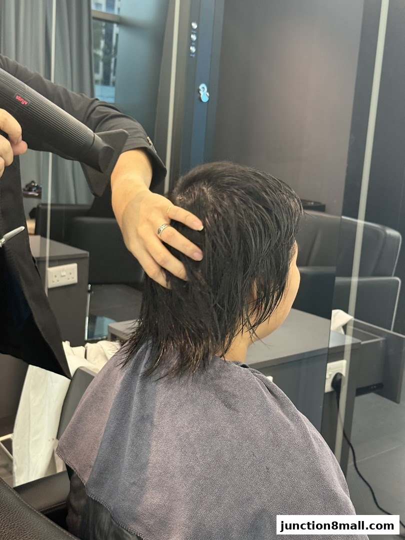 A hairstylist blow-dries a client's wet hair in a modern salon setting.