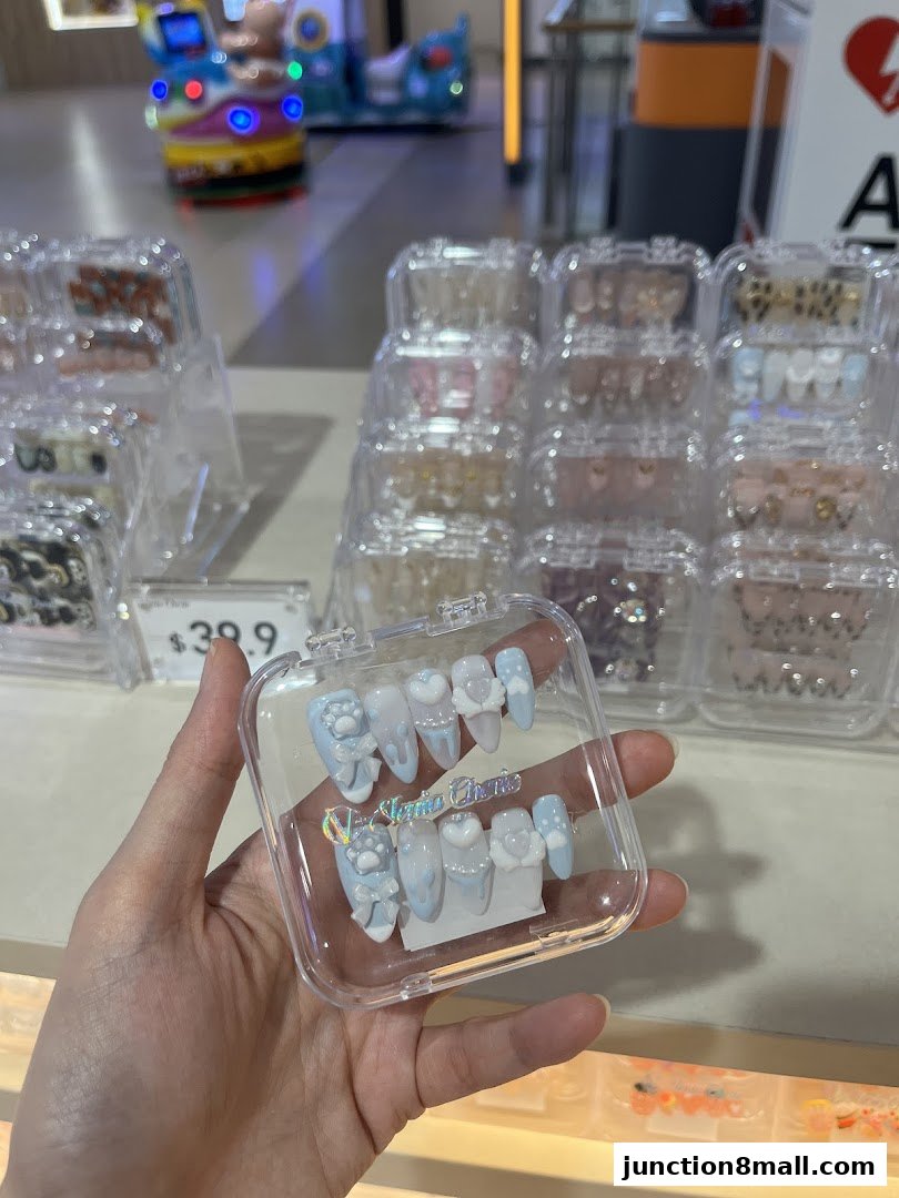 A hand holds a clear case of light blue press-on nails with paw and heart designs.