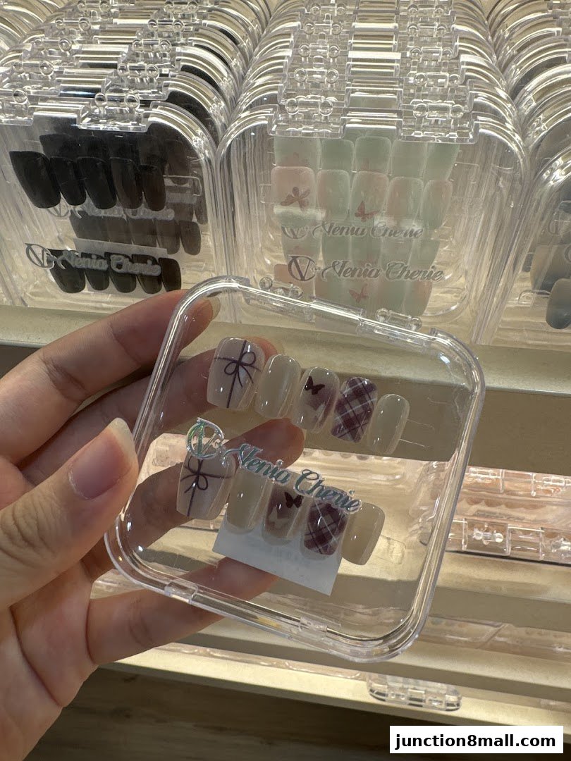 A hand holds a clear case of press-on nails with a bow and plaid design.