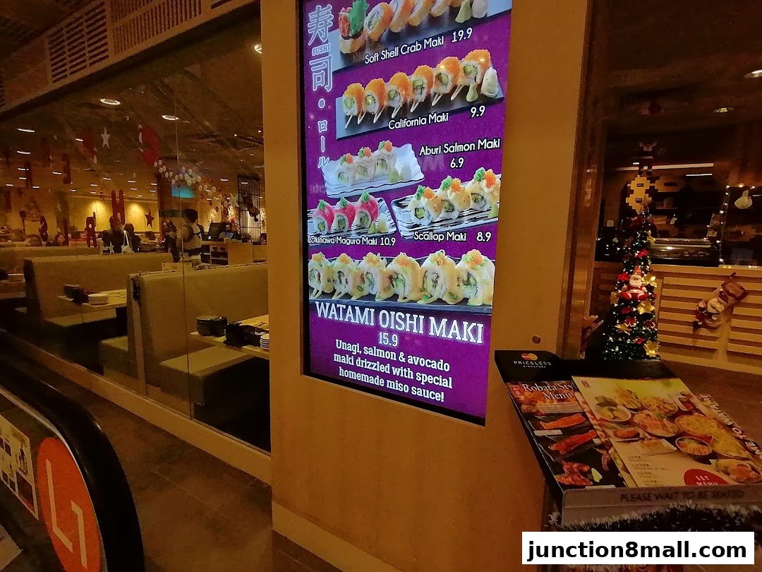 A digital menu board displays various sushi rolls with prices, next to a physical menu stand.