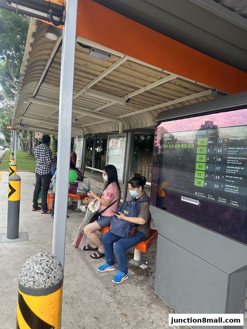 People waiting at a bus stop with a digital display showing bus arrival times.