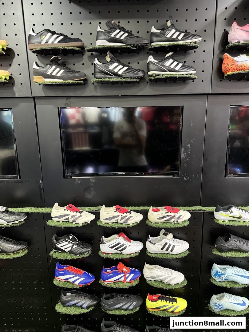 A display of various soccer cleats on shelves, with televisions mounted above.