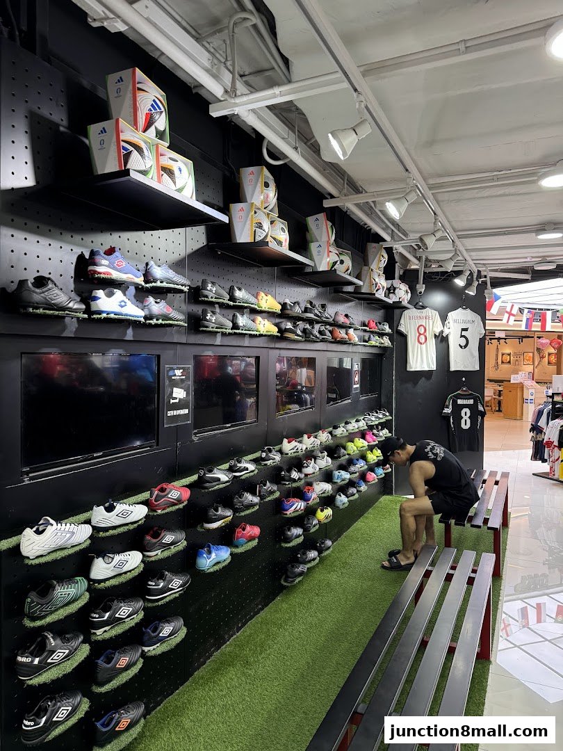 A man sits on a bench in a sports shop displaying soccer cleats and balls.