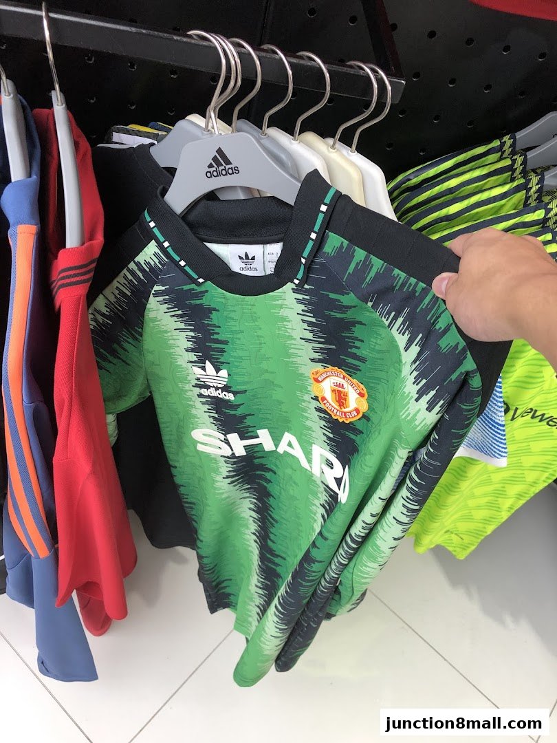 A hand holds a green Manchester United football jersey with 'SHARP' logo.