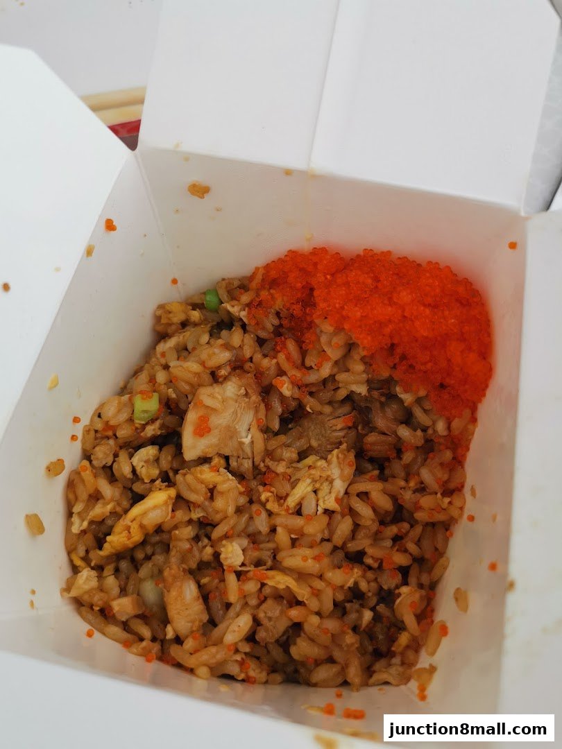 A close-up of a takeaway box filled with fried rice, chicken, and tobiko.