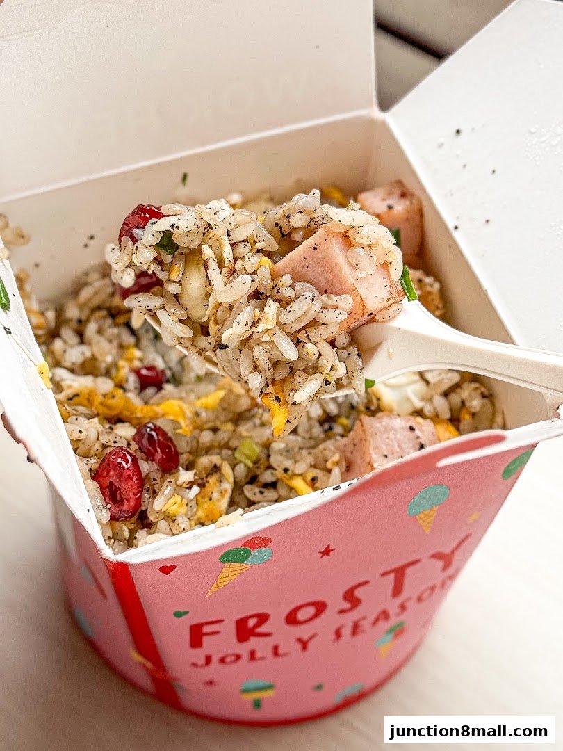 A close-up of a takeaway box filled with fried rice, ham, and cranberries.