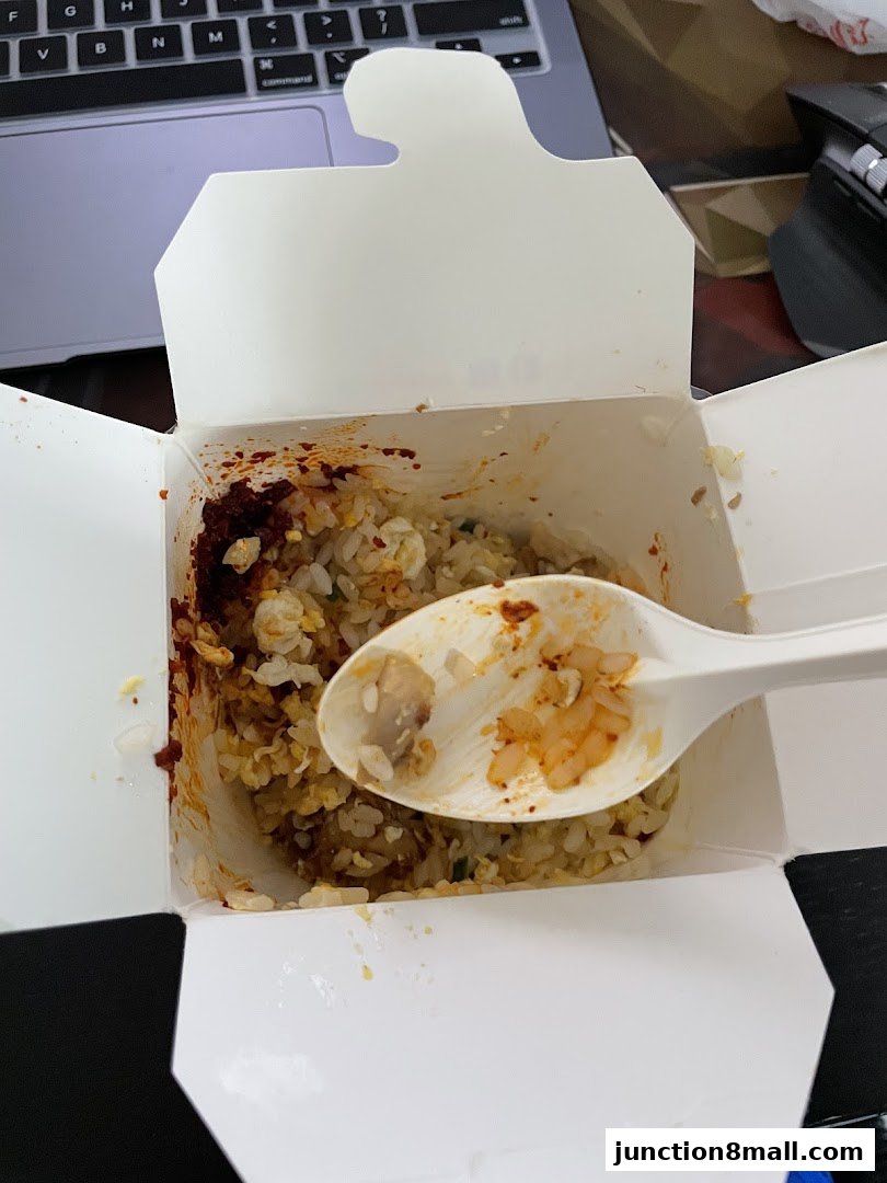 A white takeout box filled with fried rice and a spoon with food on it.