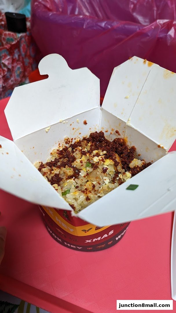 A close-up of a takeaway box filled with fried rice topped with chili flakes.