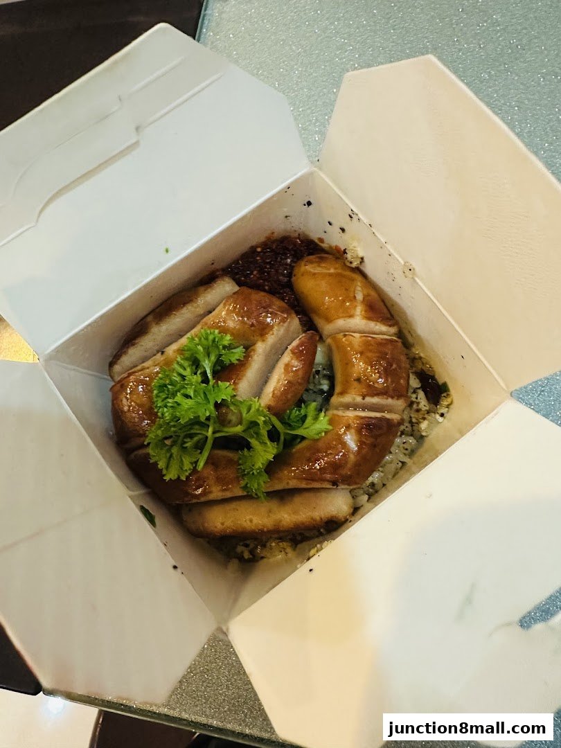 A takeaway box filled with rice, topped with sliced grilled pork and garnished with parsley.