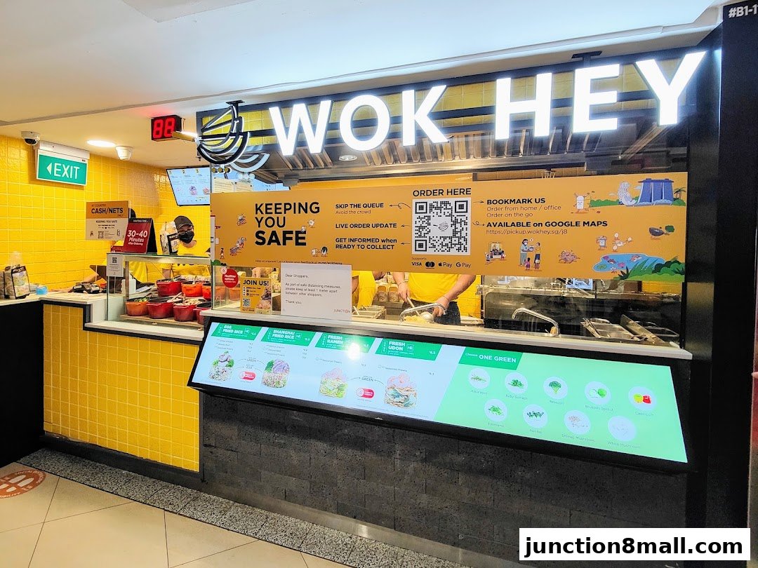 The Wok Hey shop front with bright yellow tiles and a digital menu displaying food options.
