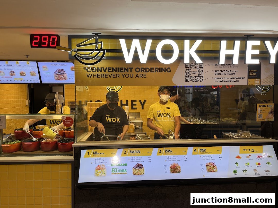 Wok Hey staff preparing food behind a counter with a digital menu and ordering information.