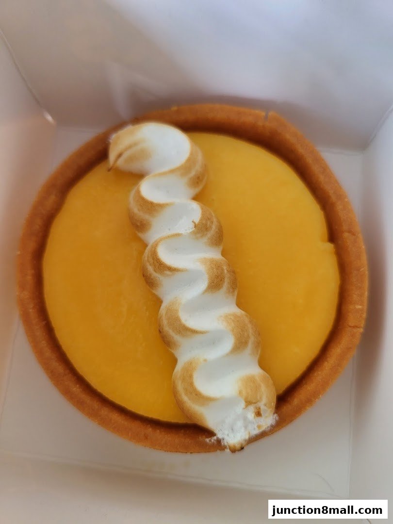A close-up of a lemon tart with torched meringue in a white box.