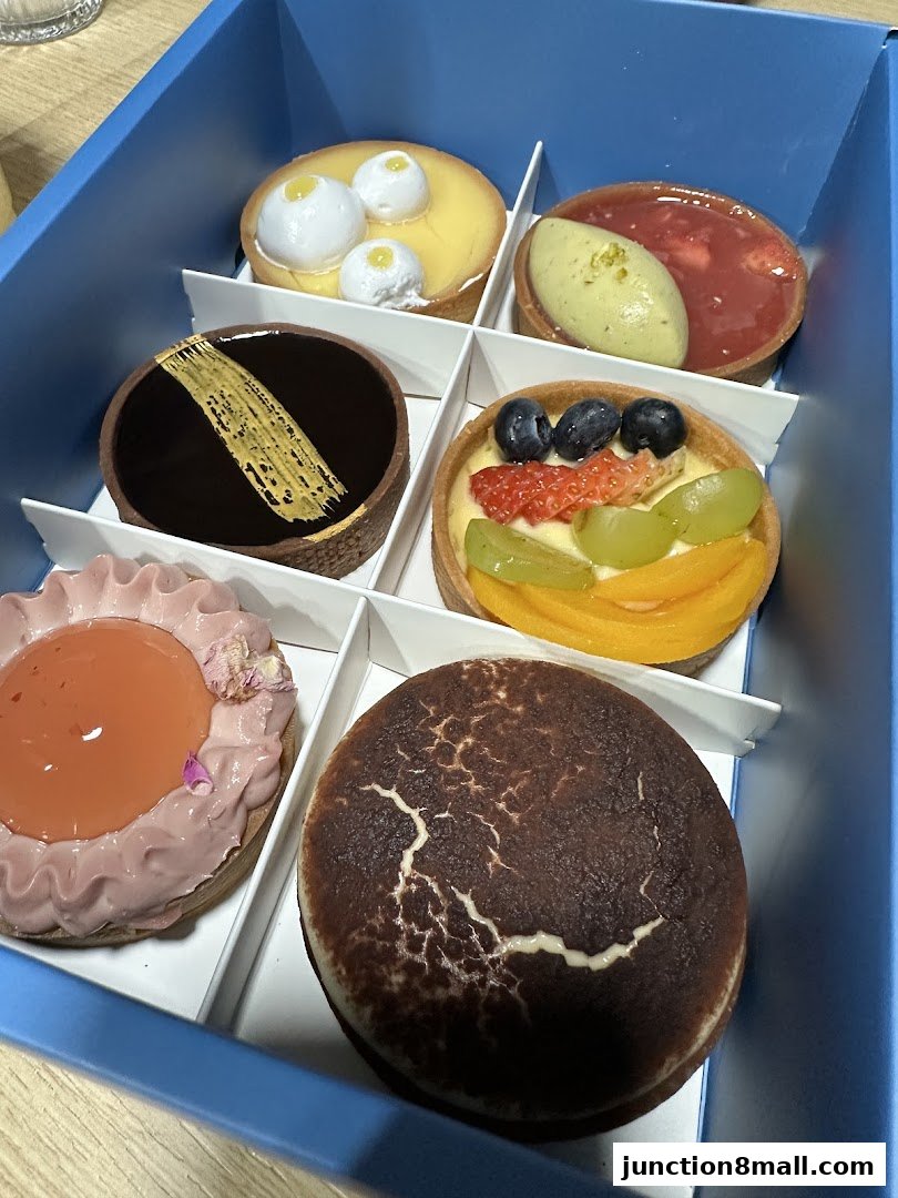 A blue box filled with six assorted gourmet tarts, each uniquely decorated.