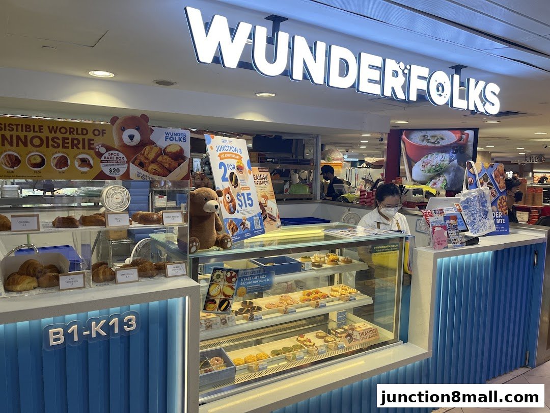 A brightly lit pastry shop counter displaying a variety of tarts and baked goods, with staff serving customers.