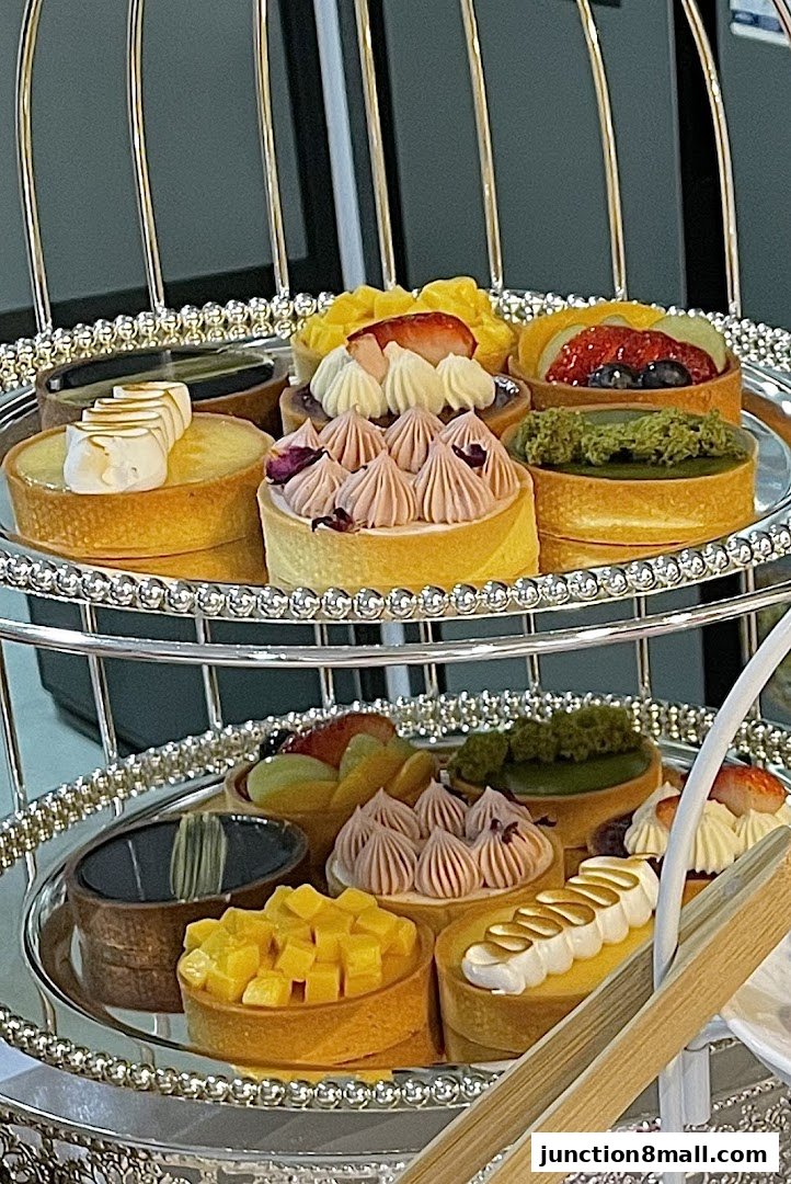 A tiered silver stand displaying a variety of beautifully decorated tarts with fruit and cream toppings.