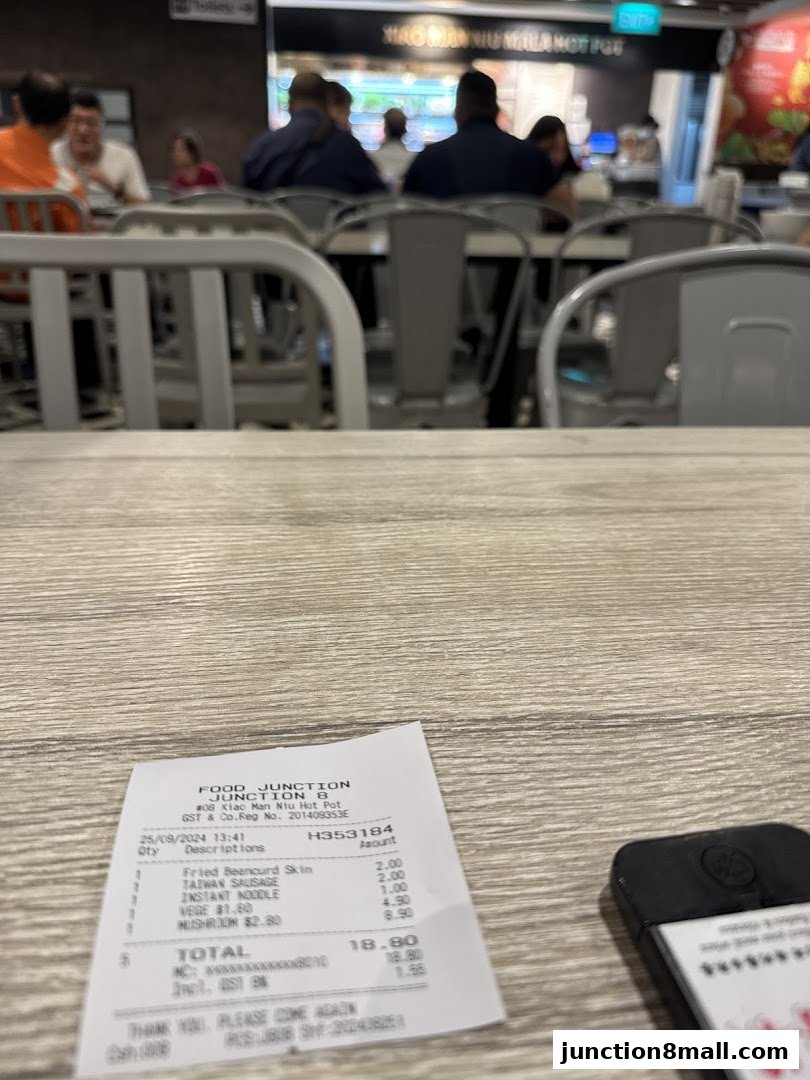 A receipt from Xiao Man Niu Mala Hot Pot is placed on a wooden table with blurred diners in the background.