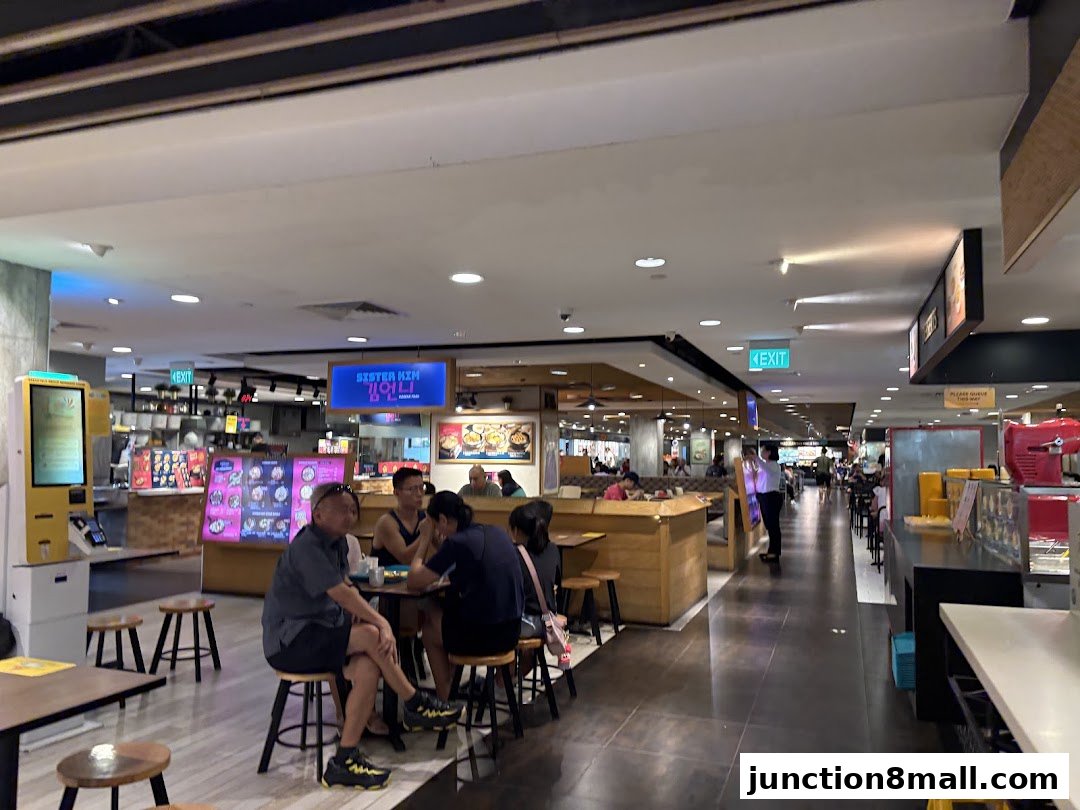 People dining at tables in a food court with various food stalls visible.