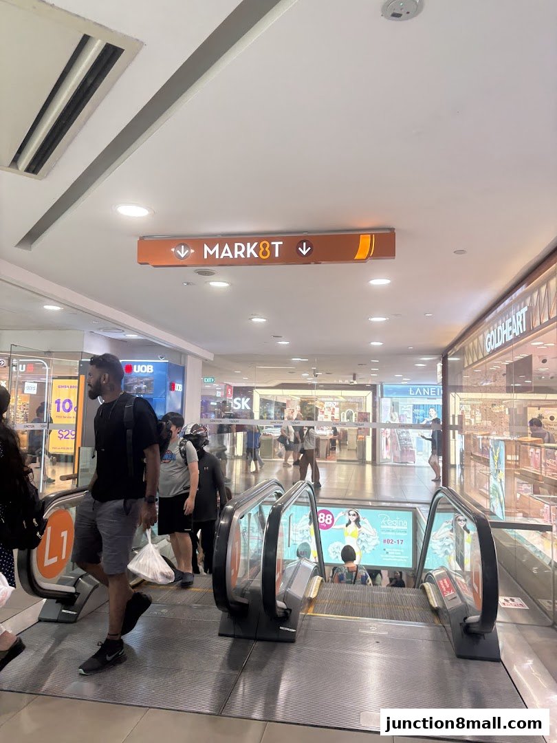 People on escalators in a shopping mall with directional signs and shop fronts.