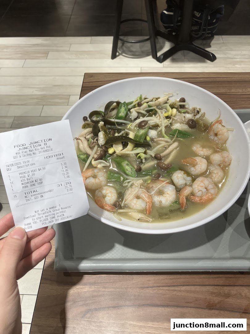 A bowl of mala hot pot with shrimp and vegetables, next to a receipt.