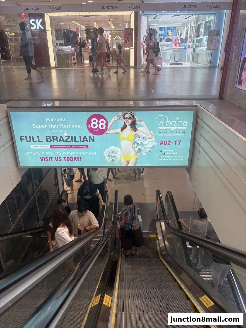 An advertisement for a hair removal service is displayed above escalators in a shopping mall.