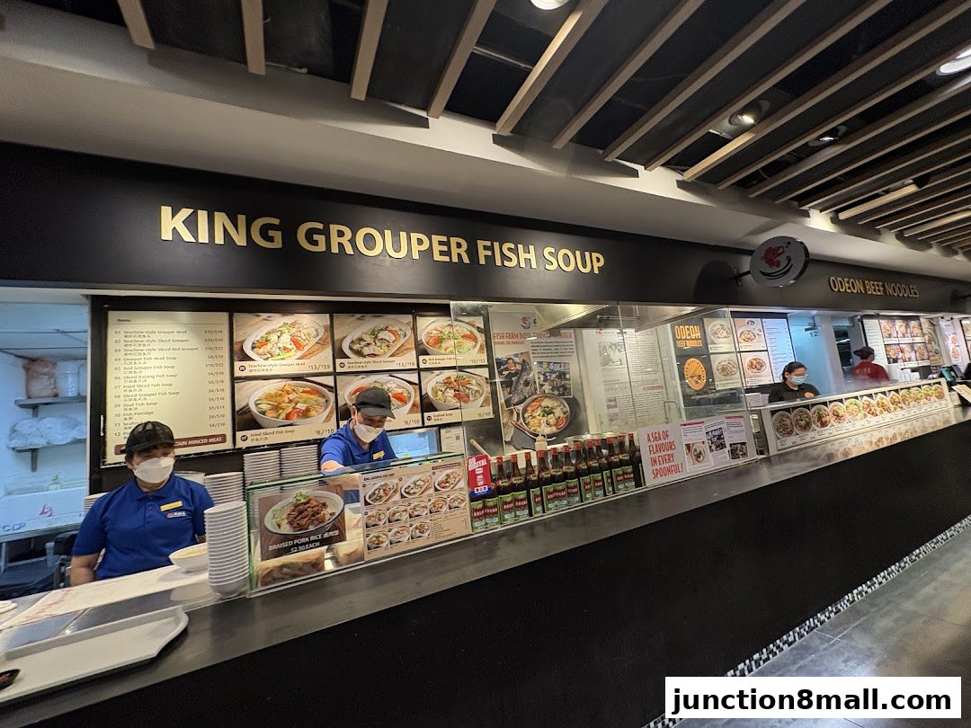 A food stall counter displaying a menu for King Grouper Fish Soup and Odeon Beef Noodles.