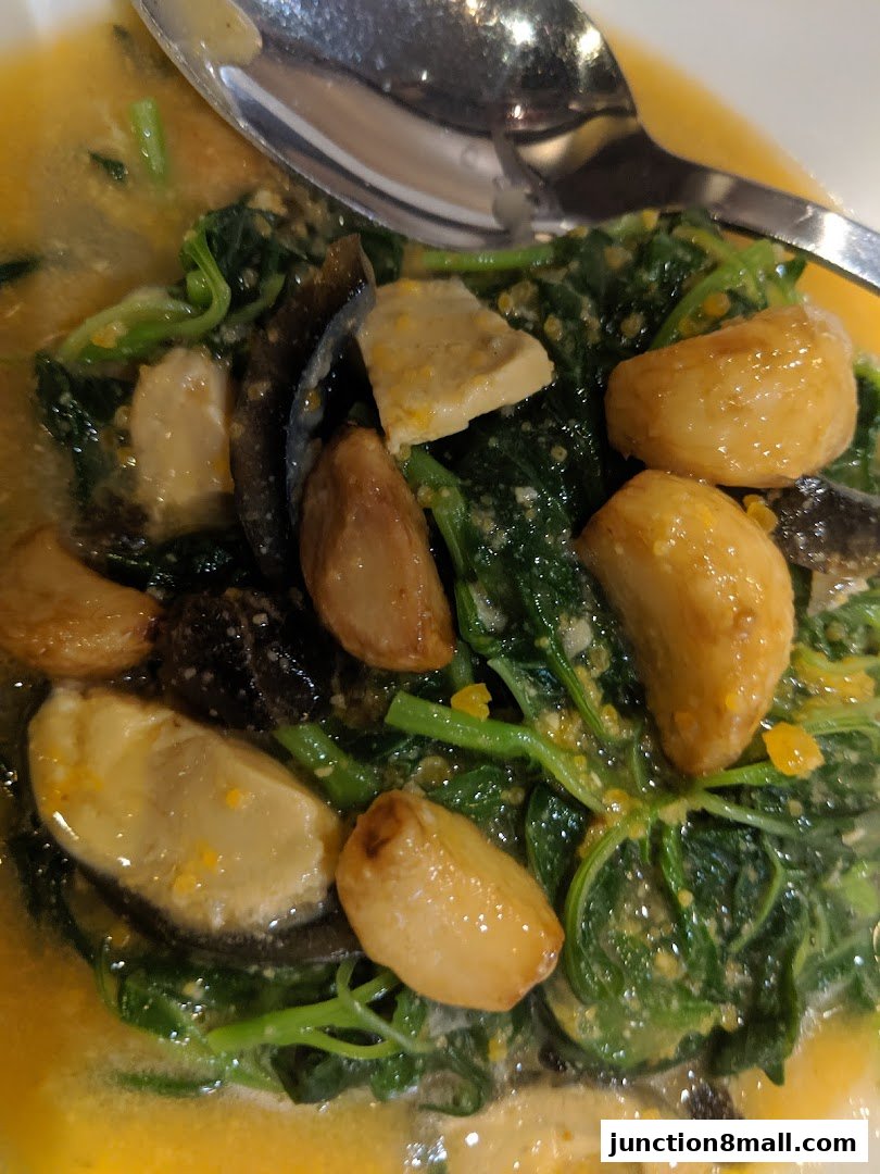 A close-up shot of a dish with leafy green vegetables, garlic, and mushrooms in a savory sauce.