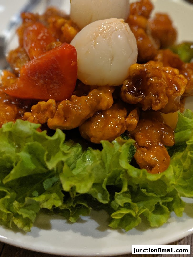 A close-up of a delicious dish with sweet and sour chicken, lychees, and lettuce.
