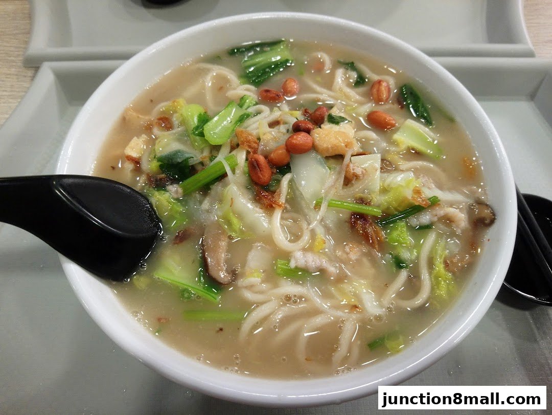 A close-up shot of a steaming bowl of noodle soup with vegetables and peanuts.