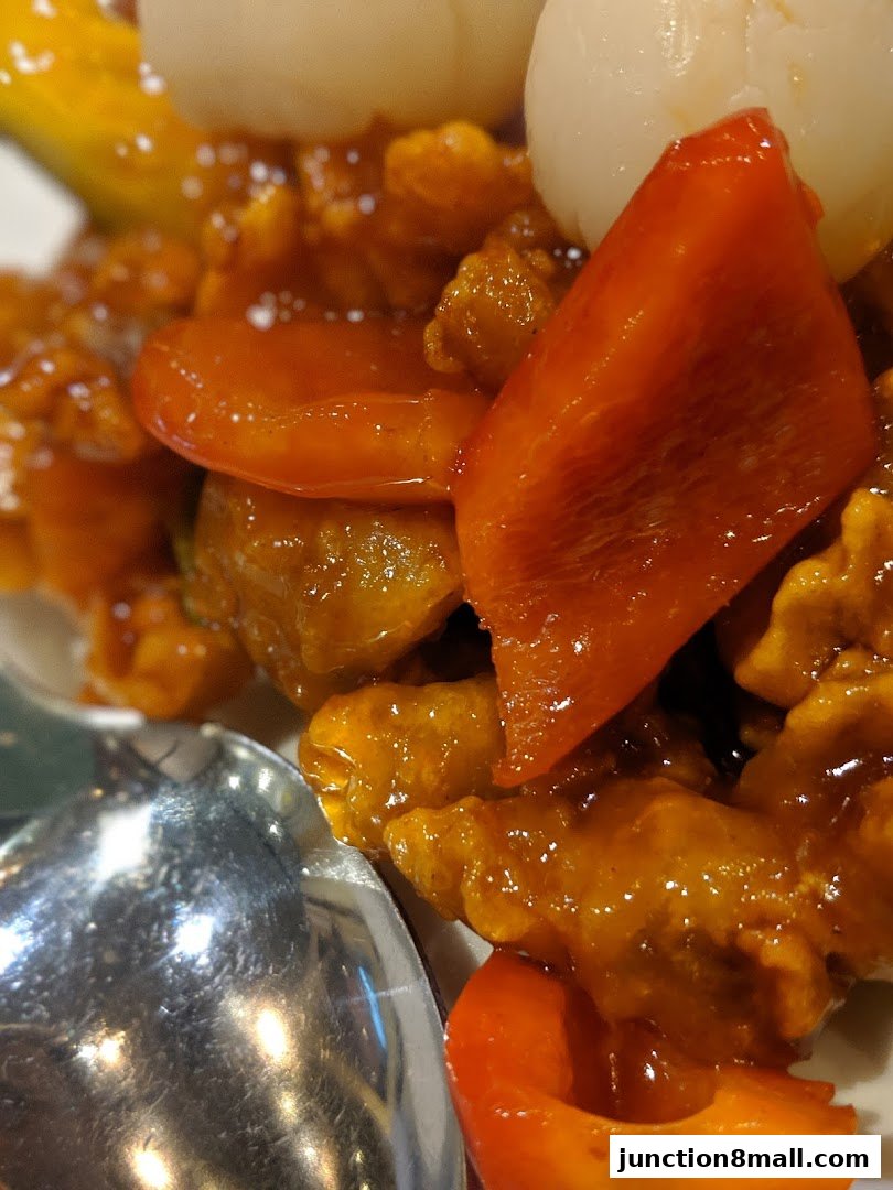 A close-up of a delicious dish with sweet and sour sauce, bell peppers, and lychees.