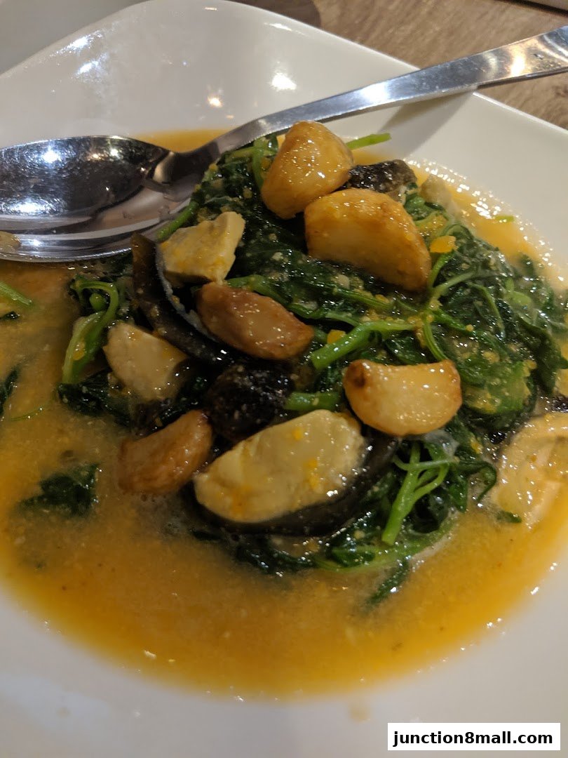 A close-up of a dish with leafy greens, garlic, and sauce, served on a white plate.