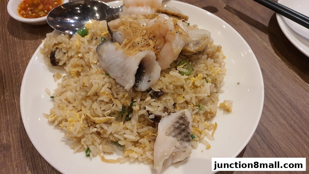 A plate of seafood fried rice with fish, shrimp, and scallops, served with chili sauce.