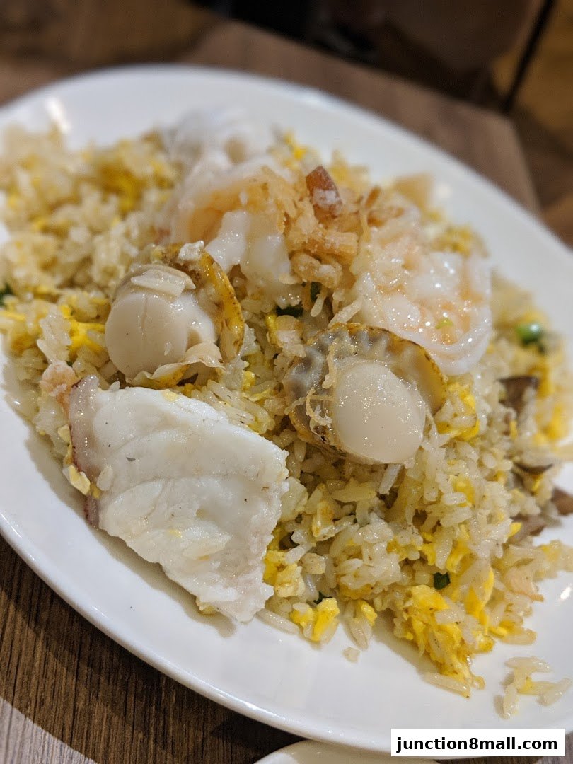 A plate of seafood fried rice with scallops, shrimp, and fish.