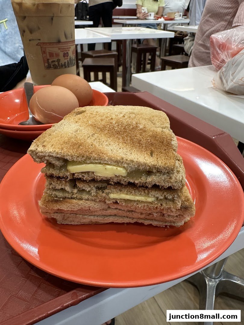 A close-up of Ya Kun Kaya Toast's signature kaya toast with butter, served with soft-boiled eggs and iced coffee.