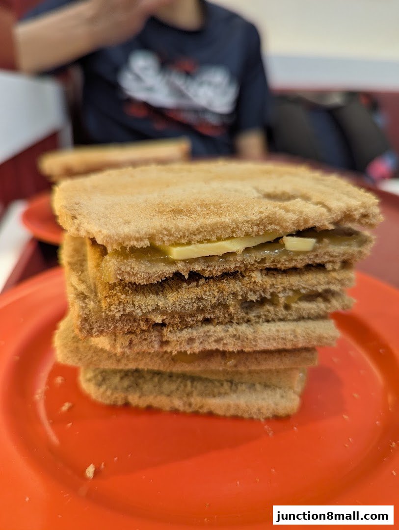 A close-up shot of stacked kaya toast with butter on an orange plate.