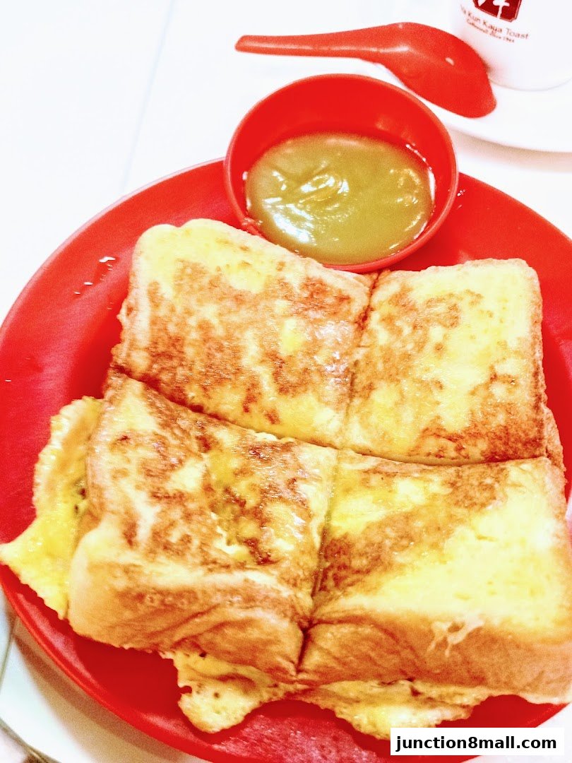 A close-up of French toast with kaya dip and a spoon on a red plate.