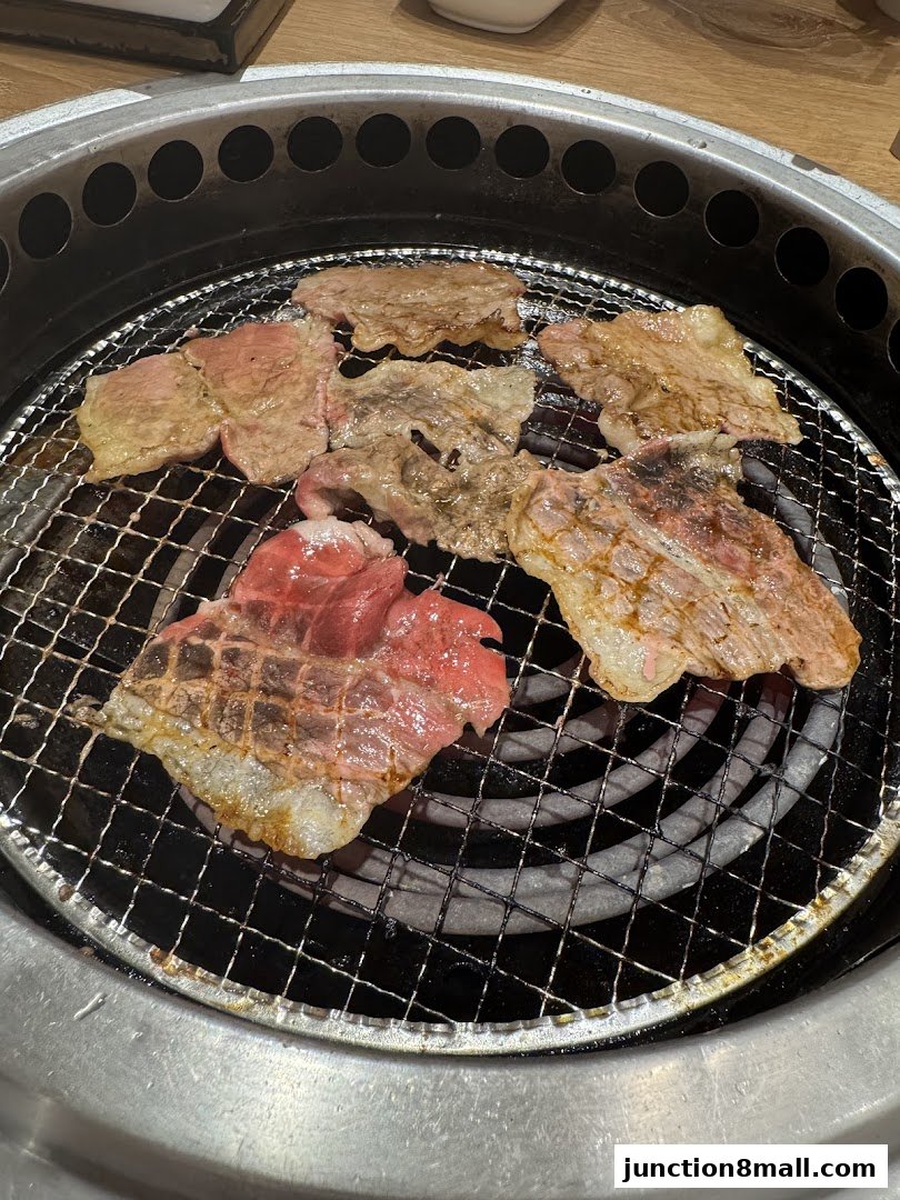 Slices of raw and grilled beef cooking on a metal grill over a heat source.