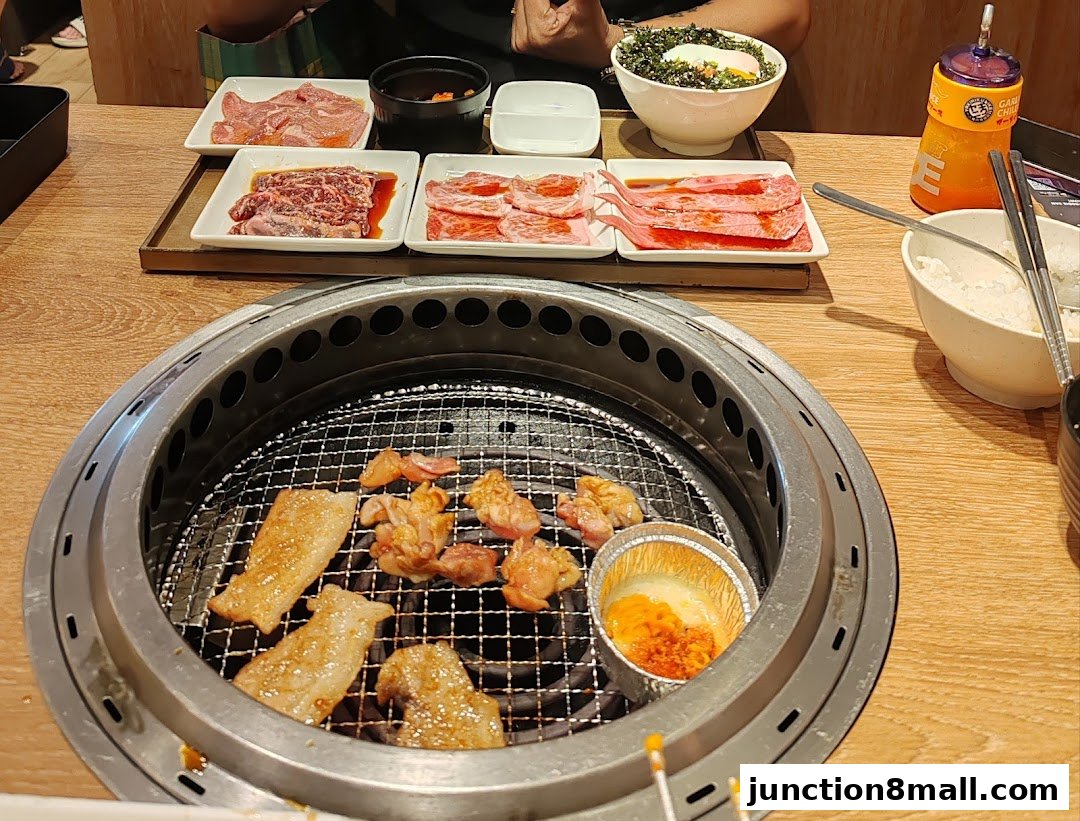 A table laden with various cuts of raw meat and grilled meats, rice, and a bowl of food.