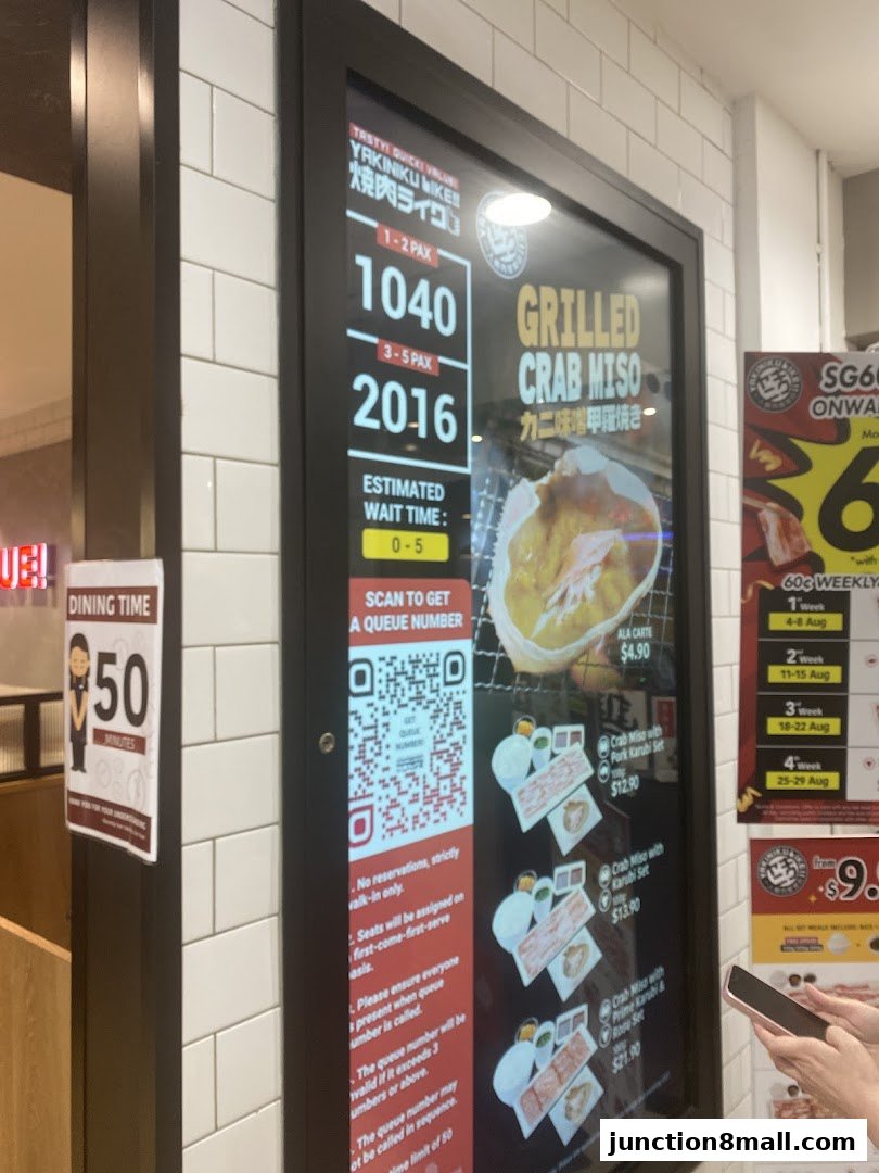 A digital display shows queue numbers, estimated wait times, and menu items for Yakiniku Like.