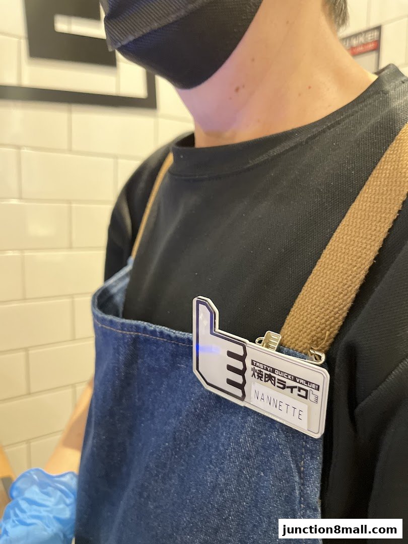 A close-up of a staff member wearing an apron with a name tag and a thumbs-up logo.